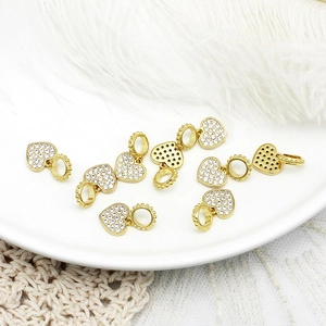 Macro detail of eight gold-plated 18k heart charms with white zircon pavé on ceramic surface