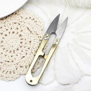 Golden U-shaped sewing thread snips shown on a white lace and plush background texture