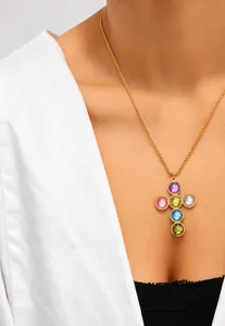 Primo piano di una collana con ciondolo a croce dorata con pietre preziose colorate su modella