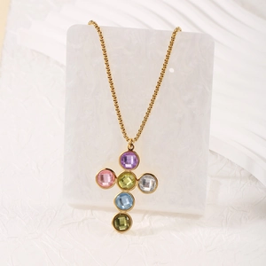 Dettaglio di una collana con ciondolo a croce dorata con sei cristalli rotondi colorati su marmo