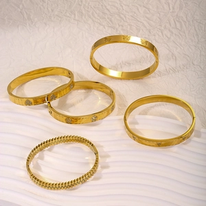 Dettaglio di 5 bracciali rigidi in acciaio inossidabile dorato con zirconi e stelle