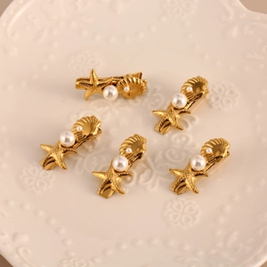 Goldenes Haarspangen-Set mit Seestern, Muschel und weißen Perlen auf Keramikteller