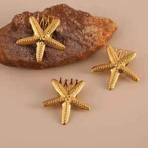 Three gold starfish hair clips with natural texture on brown rocks and beige background