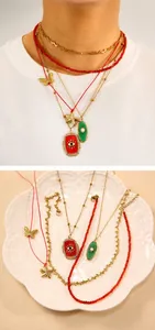 Detail of layered gold necklace with red evil eye pendant and colorful charms on white plate