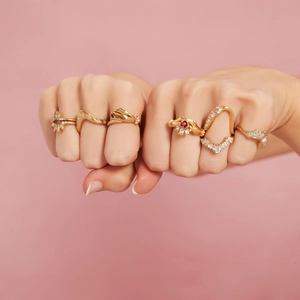 Chique gouden geometrische ringen met robijnen en zirkoon op handen met roze achtergrond