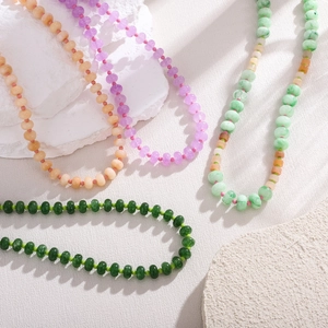 Handmade beaded necklace with natural pink and green stones displayed on white textured stone