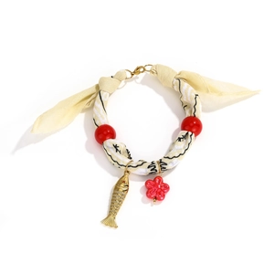 Detail of floral silk anklet with red beads and golden fish charm on white background