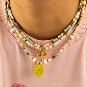 Collana artigianale di perline con ciondolo a fungo dorato e uva gialla su t-shirt rosa