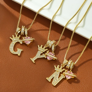 Close-up of crown initial necklaces with pink heart planet charms in golden finish