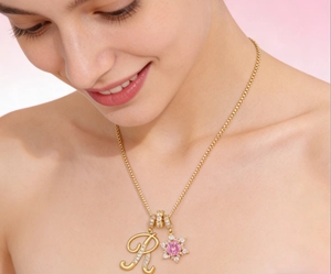 Detalle de collar de bolas chapado en oro 18K con colgante rosa y letra R de circonitas