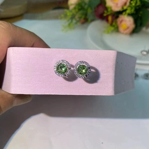 Vue macro détaillée des boucles d'oreilles argentées avec zircon vert émeraude et halo diamants