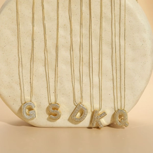 Makroansicht goldener Buchstabenketten mit Zirkonia-Einlage auf einem Keramikständer