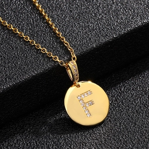 Detalle macro de collar chapado en oro con colgante de letra F y cristales sobre fondo negro