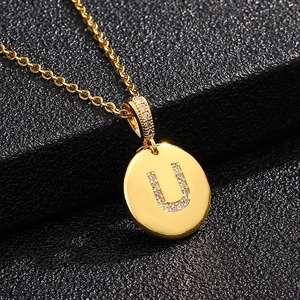 Detalle de un colgante de disco dorado con la letra U de circonita cúbica y cadena fina