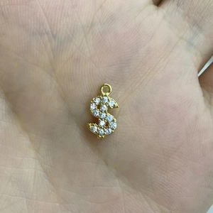 Gros plan d'un pendentif signe dollar doré avec zircons pavés scintillants sur main