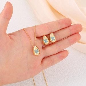 Close-up of golden teardrop jewelry set featuring blue butterfly enamel details and crystals