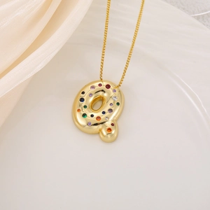 Macro d'un pendentif lettre Q dorée serti de zircons colorés sur fond de soie