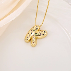 Vue détaillée du pendentif lettre K doré avec zircons multicolores sur soie blanche