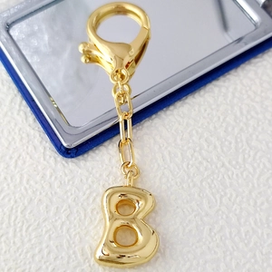 Macro shot of 18K gold plated bubble letter B keychain with lobster clasp on textured surface