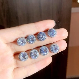 Close-up of hand holding four pairs of round halo cubic zirconia stud earrings in silver