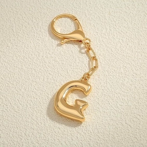 Dettaglio macro del portachiavi lettera G placcato oro 18K con finitura in metallo lucido
