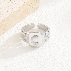 Detail eines silbernen geometrischen quadratischen Rings mit Zirkon-Buchstabe C und offenem Band