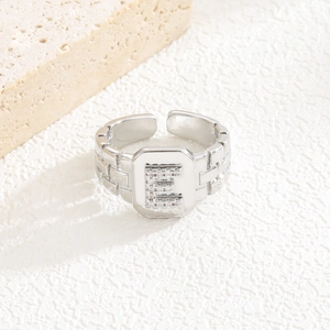 Makroaufnahme eines silbernen Rings mit Zirkonia-Buchstabe E und Backstein-Textur