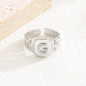 Makro-Detail des silbernen verstellbaren Rings mit Zirkonia-G-Buchstaben und Kettenstruktur