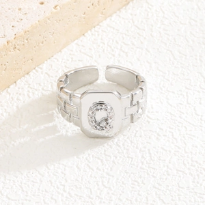 Nahaufnahme von silbernem Ring mit quadratischer Textur und Zirkonia-Buchstabe Q
