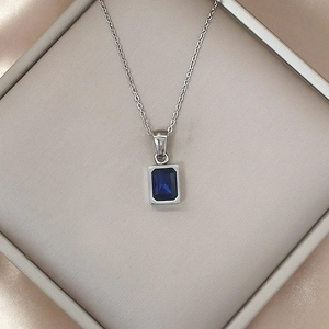 Close-up of a blue rectangular zircon pendant on a silver chain in a luxury jewelry box