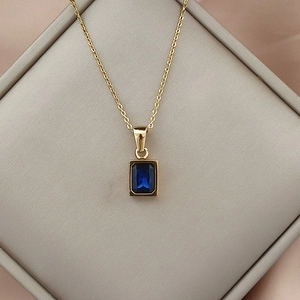 Detail of gold necklace featuring a blue square zircon pendant on pink satin
