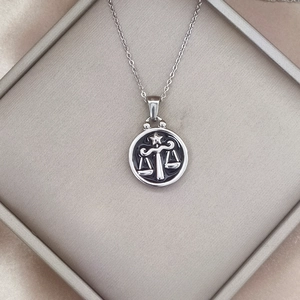 Macro view of Libra zodiac pendant in vintage silver finish with embossed scale design