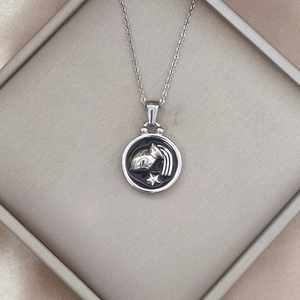 Detailed close-up of a silver zodiac pendant with silver embossing on a black background