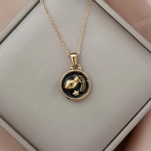 Macro shot of gold Aquarius zodiac pendant with black enamel inlay on grey jewelry box