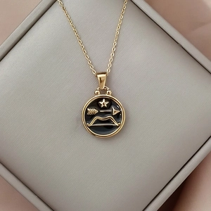 Close-up of golden zodiac pendant with black enamel and star bow design in a gift box