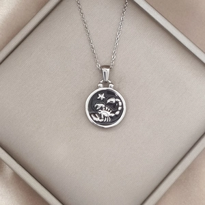 Detailed view of silver Scorpio zodiac pendant with black enamel on silk fabric