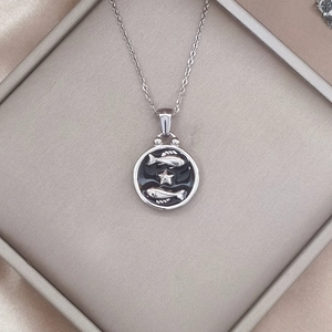 Detailed macro view of Pisces zodiac pendant on black enamel background with silver chain