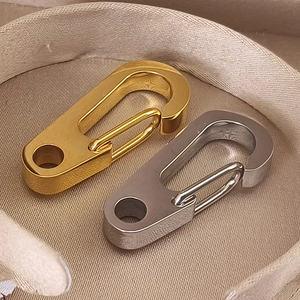 Nahaufnahme von polierten Edelstahl-Karabinern in Gold und Silber auf beigem Stoff