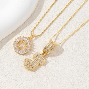 Close-up of gold J-pendant necklaces with iced-out baguette cubic zirconia settings