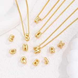 Makroaufnahme der polierten goldenen Bubble-Buchstaben-Anhänger und Halskette mit Glanz