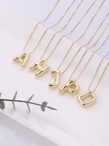 Detailopname van 18K vergulde ballonstijl letterhangers aan fijne schakelkettingen