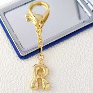 Polished 18K gold letter R keychain with large lobster clasp on white marble surface
