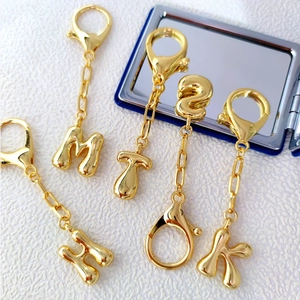 Macro detail of 18K gold-plated bubble letter charms with glossy metallic finish and clasp