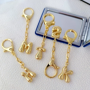 Close-up of 18K gold-plated bubble letter keychains featuring M, H, T, S, K initials