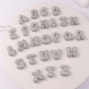 Macro view of gold-plated bubble initial pendants set with cubic zirconia on a white tray