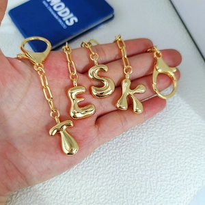 Detail of 18K gold bubble letter pendants T, E, S, K held in hand to show scale