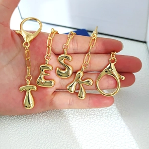Detailed macro view of gold bubble letter pendants with lobster clasps and shiny finish