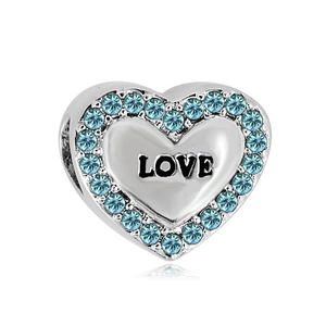 Macro view of a heart-shaped silver bracelet charm with blue crystals and LOVE engraving