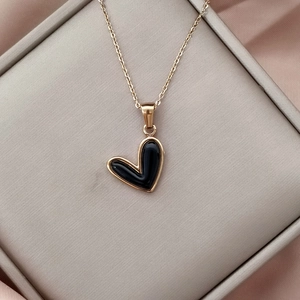 Primer plano de colgante de corazón negro con borde dorado en seda dentro de un joyero