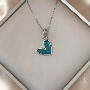 Primer plano del collar con colgante de corazón de esmalte azul en caja de seda